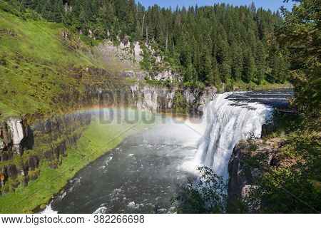 A Rainbow In The Mist Of Upper Mesa Falls As It Cascades Over A Cliff In The Rugged Wilderness Of He