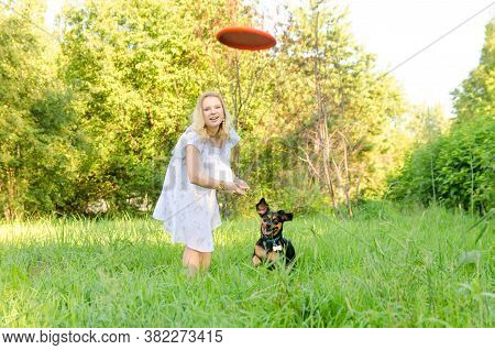 A Beautiful Blonde Young Woman Throws A Frisbee After Which A Dog Runs.