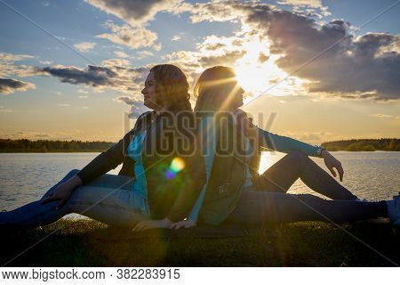 Two Girls Friends, Sisters, Cousins Socializing And Having Fun On The Shore Or Beach Of A Lake Or Ri