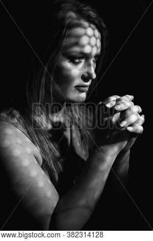 Beautiful woman confesses in the confessional, black and white. Praying woman, fine art portrait with interesting ligth and shadow pattern. Absolution. 