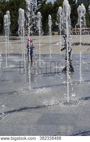 Nikolaev, Ukraine - August 17, 2020: Children Rollerblading Among The Jets Of The Fountain. Water Je