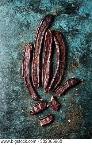 high angle view of some ripe carob beans on a rustic dark green surface