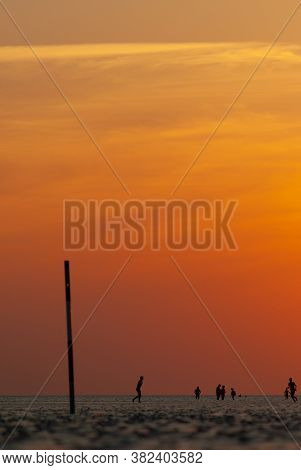 People On The Beach Around A Pole In The Sunset In The Wadden Sea.