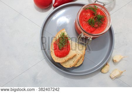 Ajvar (pepper Mousse) In A Jar And On Gray Plate With Bread And Gray Backgground. Ajvar - Delicious 