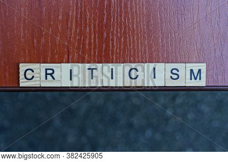 Word Criticism Made Of Wooden Square Letters On Brown Table On A Gray Background