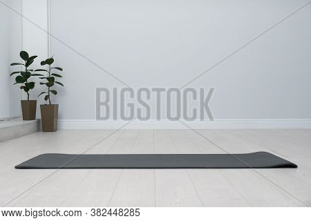 Unrolled Black Yoga Mat On Floor In Room. Space For Text