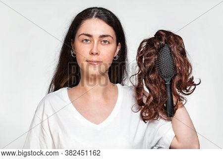 Portrait Of A Pretty Woman Holds A Comb With A Wig On It. White Background. Concept Of Hair Care And
