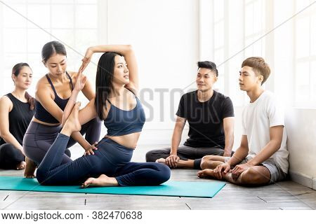 Asian people learning Yoga class in fitness club. Instructor coaching and adjust correct pose on king pigeon pose to student at front while others looking. Yoga Practice Work out lifestyle concept.