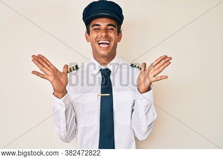 Young hispanic man wearing airplane pilot uniform celebrating mad and crazy for success with arms raised and closed eyes screaming excited. winner concept 