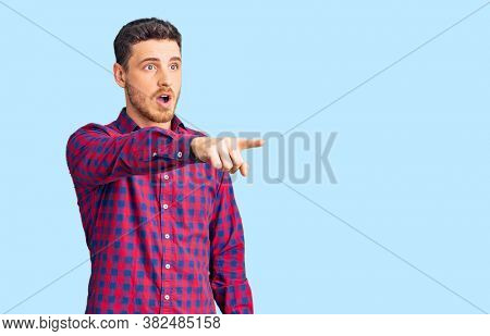 Handsome young man with bear wearing casual shirt pointing with finger surprised ahead, open mouth amazed expression, something on the front 