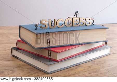 Miniature Construction Builders Working Around The Golden Heading Succcess On Top Of A Stack Of Book