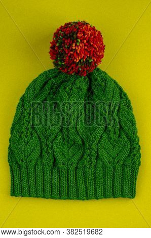 Beautiful Kace Handknitted Hat With Multicolored Pompon On Yellow Background. Top View