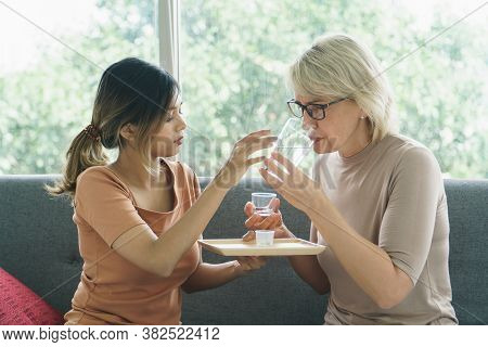 Asian Growing Daughter Giving Medical Pill With  Glass Of Water, Sick Older Caucasian Mother.concept