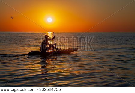 Silhouette Of A Man Floating On A Board With An Oar. Dawn Sun On The Sea. Swimming On A Supboard. Wa