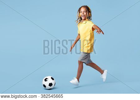 Happy Little Boy With African Dreads Shoot Soccer Ball Over Blue Background.