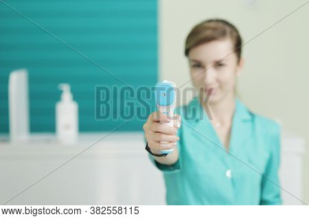 Female Doctor Or Nurse At Hospital Holds Pyrometer In Hand. Safety Measures Against The Coronavirus.