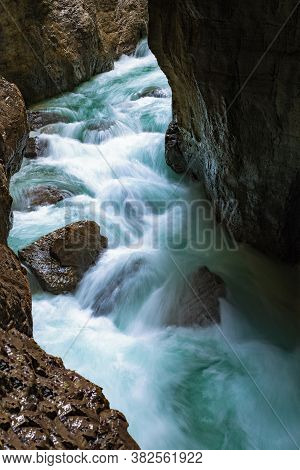 Stormy Mountain Stream With Clear Blue Water Flows Down A Rocky Gorge In Partnachklamm In Germany. S