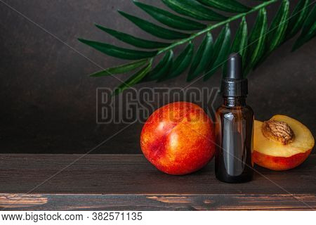 Bottle Of Peach Oil, Decorated With Peaches On Wooden Table And Dark Borwn Background. The Concept O