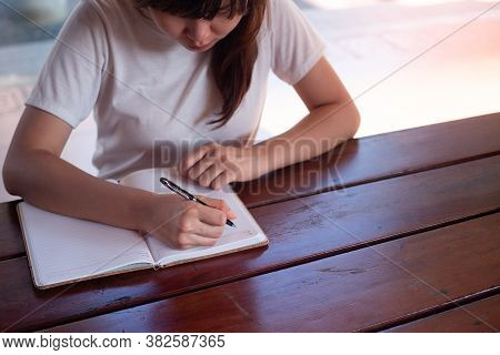 Image Of A Woman Writing On A Blank Notebook On The Table.