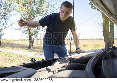 The Man Checks The Oil Level. Male Hands Hold A Dipstick, Which Shows The Level Of Engine Oil. Serio