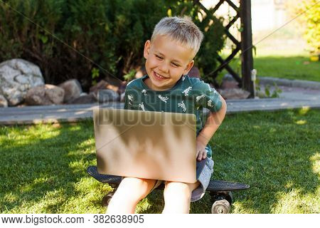 The Boy Is Sitting On The Grass And Studying On A Laptop. Concept Of Remote Learning, Home Learning,