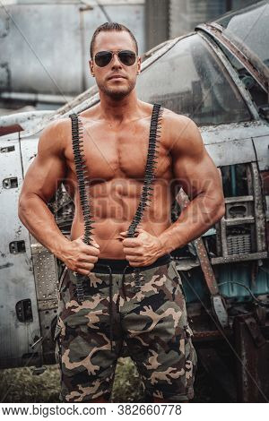 Muscular American Soldier With Stationary Airplane Behind. Brutal Man With Large Biceps And Naked To