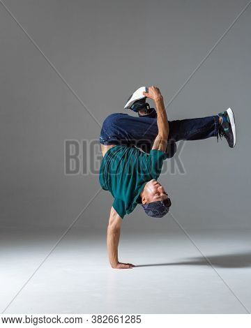 Cool Guy Breakdancer Dance On The Floor Standing On One Hand Isolated On Gray Background. Breakdance