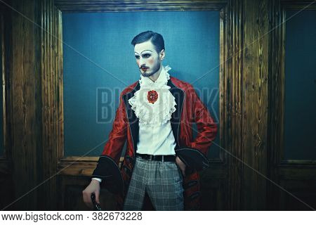 Art, history and fashion. Sophisticated young man with make-up and clothes in the style of the Rococo and Baroque eras in a rich vintage interior.