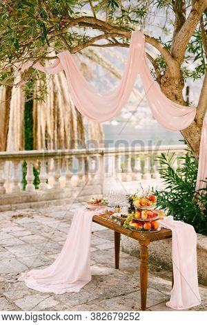 Wooden Table Decorated With Fabric With A Shelf For Fruits And Delicacies In The Courtyard With A Tr