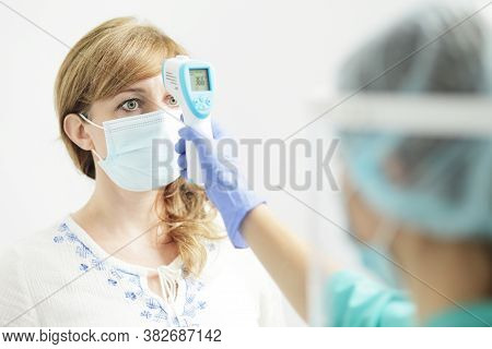 Medical Woman In Uniform Measures The Temperature Of A Woman With A Pyrometer