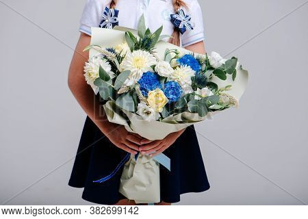A Bouquet Of Flowers, Packed In Beige Paper In The Hands Of A Girl With Pigtails On A Light Backgrou