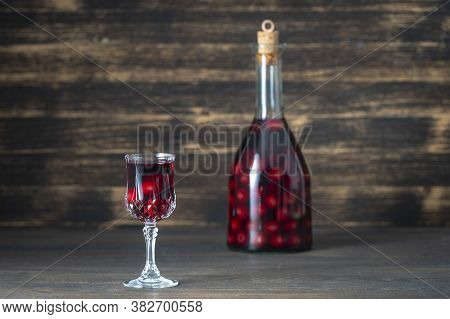 Homemade Tincture Of Red Cherry In A Glass Bottle And A Wineglass On Wooden Background, Ukraine