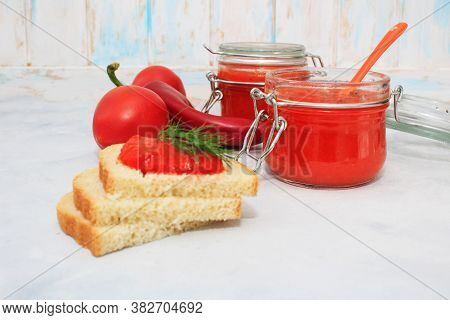 Ajvar, Pepper Mousse In A Jar And On  Bread And Gray Backgground. Ajvar - Delicious Dish Of Red Pepp