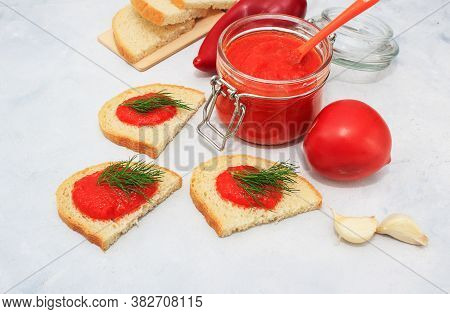 Ajvar, Pepper Mousse In A Jar And On  Bread And Gray Backgground. Ajvar - Delicious Dish Of Red Pepp