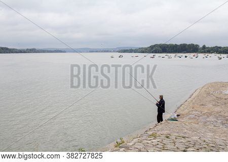 Belgrade, Serbia - July 17, 2016: Old Man, Fisherman Fishing On The Danube River During Arainy Summe