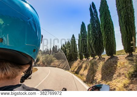 A Guy Drives A Scooter In The Streets Among The Cypresses Of The Tuscan Hills