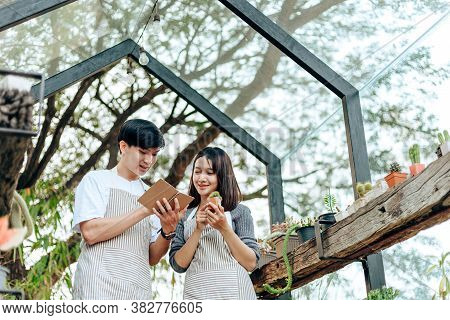 Women Hold Cactus And A Man Writing Note In A Book. Love Couple Enjoy Hobby With Darden Cactus.