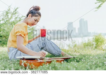 Hands Hold Coffee Cup And Write Notes,lyrics In The Book On Quitar Beside The Sea And Building City 