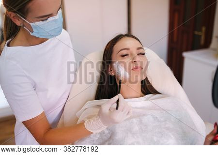 Hands Of Cosmetology Specialist Applying White Facial Mask Using Brush. Making Skin Hydrated And Fac
