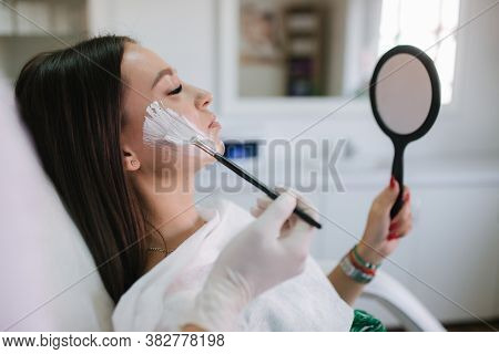 Hands Of Cosmetology Specialist Applying White Facial Mask Using Brush. Making Skin Hydrated And Fac