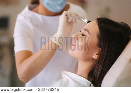 Hands Of Cosmetology Specialist Applying White Facial Mask Using Brush. Making Skin Hydrated And Fac