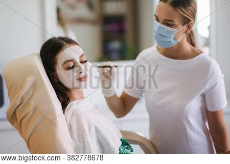 Cosmetologys Specialist Applying White Facial Mask Using Brush. Making Skin Hydrated And Face Glowin