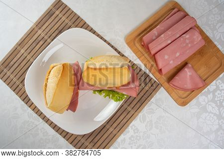 Mortadella And Lettuce Sandwich On A White Plate On A Mat And Slices Of Mortadella On The Side On A