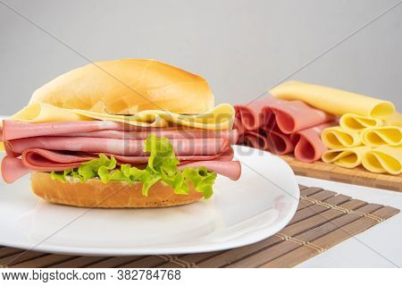 Mortadella Sandwich, Lettuce And Cheese On A White Plate On A Mat And Slices Of Mortadella And Chees