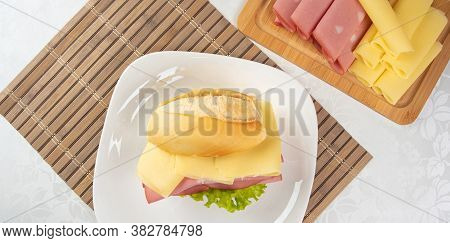Mortadella Sandwich, Lettuce And Cheese On A White Plate On A Mat And Slices Of Mortadella And Chees