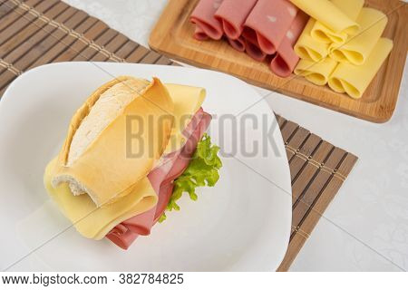 Mortadella Sandwich, Lettuce And Cheese On A White Plate On A Mat And Slices Of Mortadella And Chees