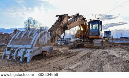Excavator During Earthmoving At Construction Site On Bluue Sky Background. Onstruction Machinery For