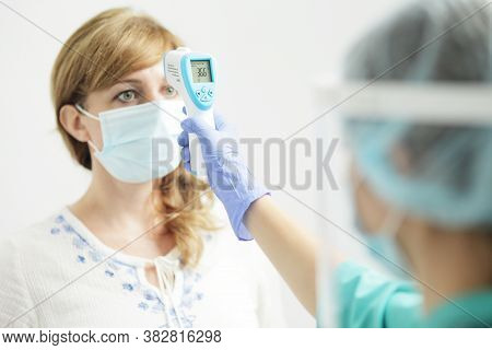 Medical Woman In Uniform Measures The Temperature Of A Woman With A Pyrometer