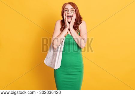 Stylish Young Rd Haired Woman In Green Dress Exclaiming In Shock, Keeping Hands On Cheeks, Astonishe