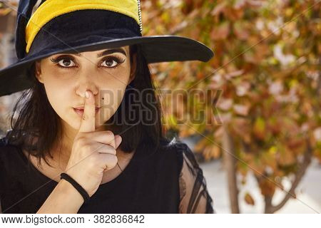Portrait Of Beautiful Female In Witch Hat Sticking Out Her Tongue And Showing Quiet Sign. Attractive